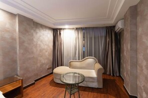 A modern living room with a sofa and a glass table, wooden flooring, and a large window with curtains. - Tianyuan Business Hotel (Baise)