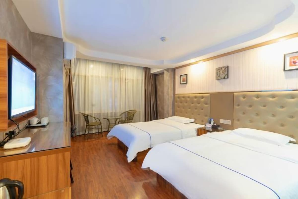 A hotel room with two beds, a desk with a computer, a TV, and a chair.