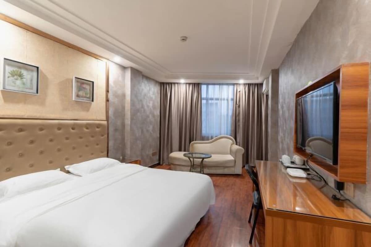 A hotel room with a large bed, a sofa, a small table, a TV, and a mirror.