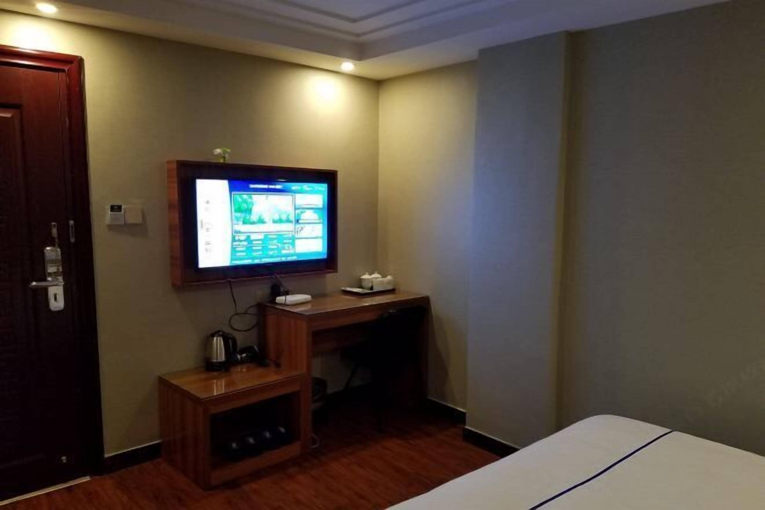 Une chambre d’hôtel avec un bureau en bois, un téléviseur fixé au mur et un lit doté d’une tête de lit blanche.