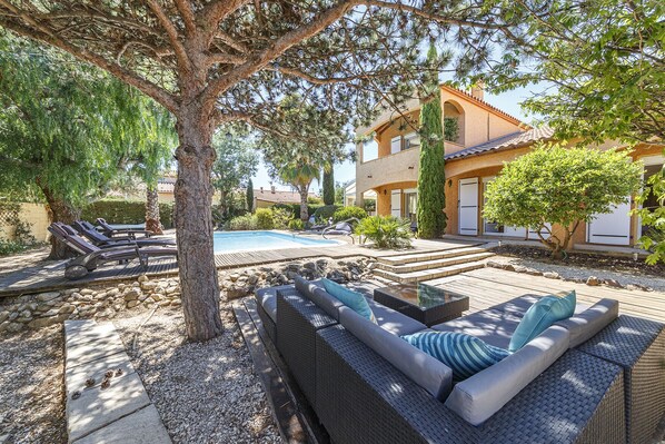 A poolside area with outdoor seating, a swimming pool, and a building with a tiled roof.