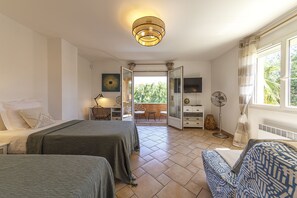A bedroom with two beds, a desk, a chair, a TV, and a balcony with a view.
