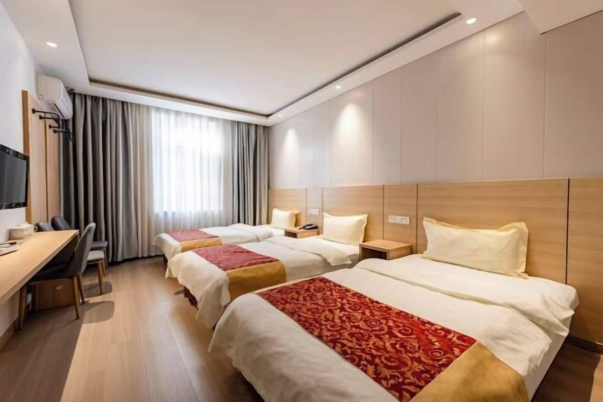 Quarto de hotel com três camas, uma mesa e uma televisão.
