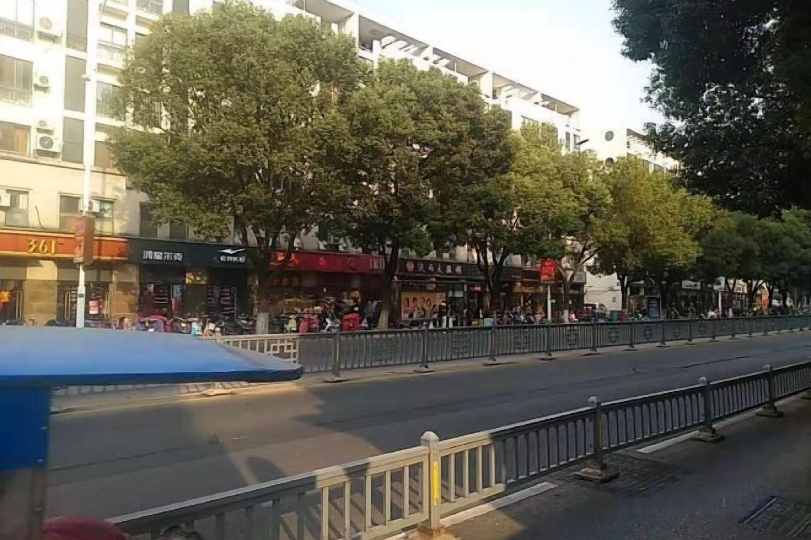 A street with storefronts, trees, and a blue vehicle.