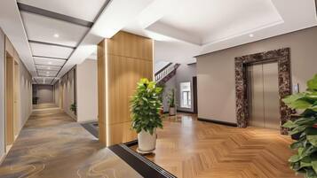 Un vestíbulo de hotel con piso de madera, una recepción, una escalera y un ascensor.