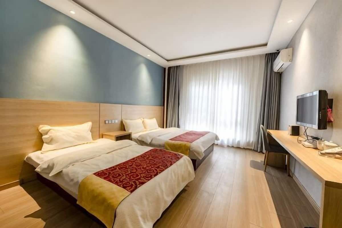 Quarto de hotel com duas camas, uma escrivaninha, televisão e uma janela grande com cortinas.