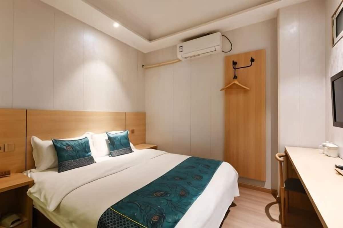 Quarto de hotel com cama, mesa de cabeceira, escrivaninha e um cabideiro.