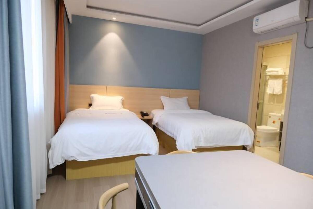Quarto de hotel com duas camas de solteiro, uma mesinha e um banheiro visível por uma porta aberta.