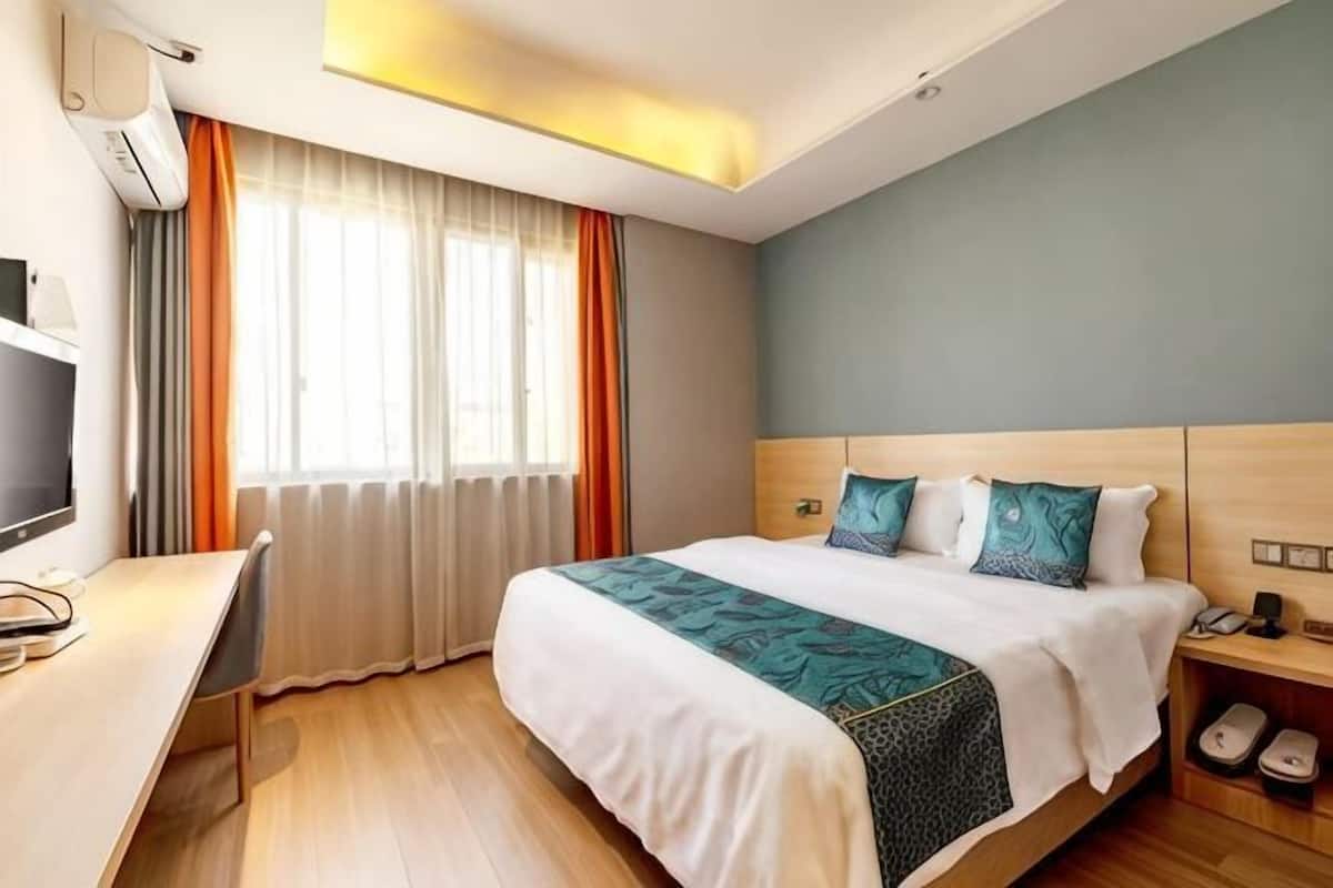 Quarto de hotel com cama, escrivaninha, televisão e sapateira.
