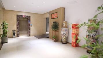 Un hall d’hôtel avec un comptoir d’accueil, un grand vase et une plante en pot.