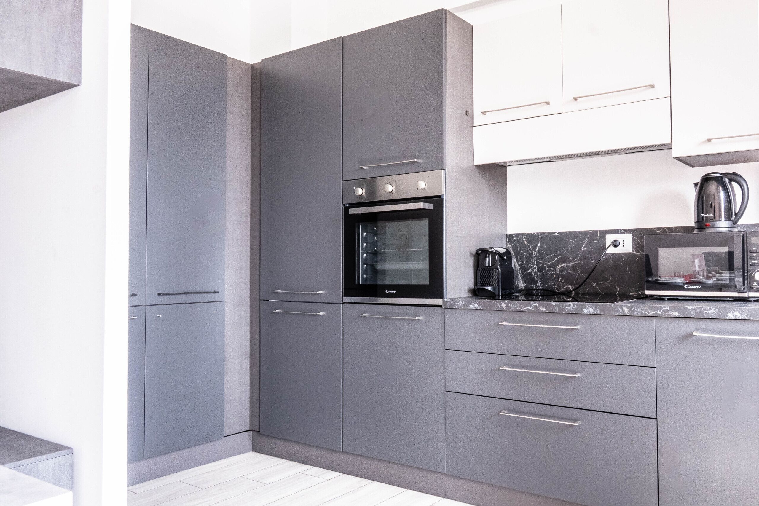 A modern kitchen with grey cabinets, a built-in oven, a coffee maker, and a microwave.