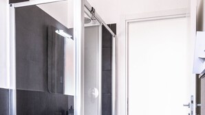 A modern bathroom with a glass-enclosed shower, a white sink, and a door leading to another room.