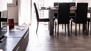 A modern kitchen with a dining area, a view through the window, and a hanging light fixture.