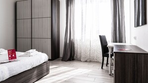 A modern hotel room with a bed, a desk, a chair, and a wardrobe.