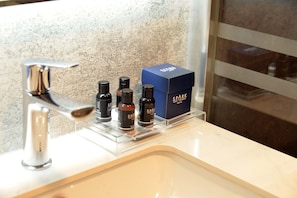 Un lavabo de salle de bain avec un robinet chromé, un miroir et une étagère sur laquelle se trouvent plusieurs petites bouteilles et une boîte bleue portant l'inscription « SPARK ».