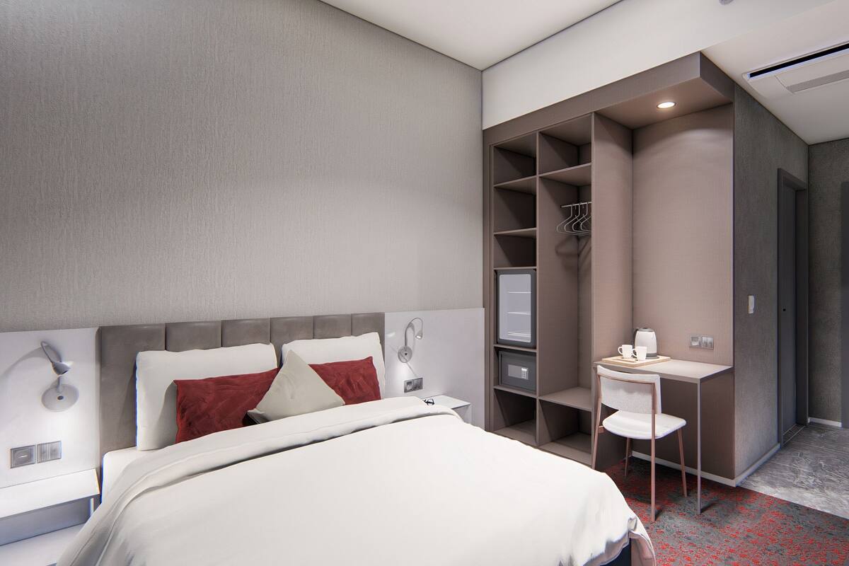 A modern hotel room with a bed, a desk, and a wardrobe.