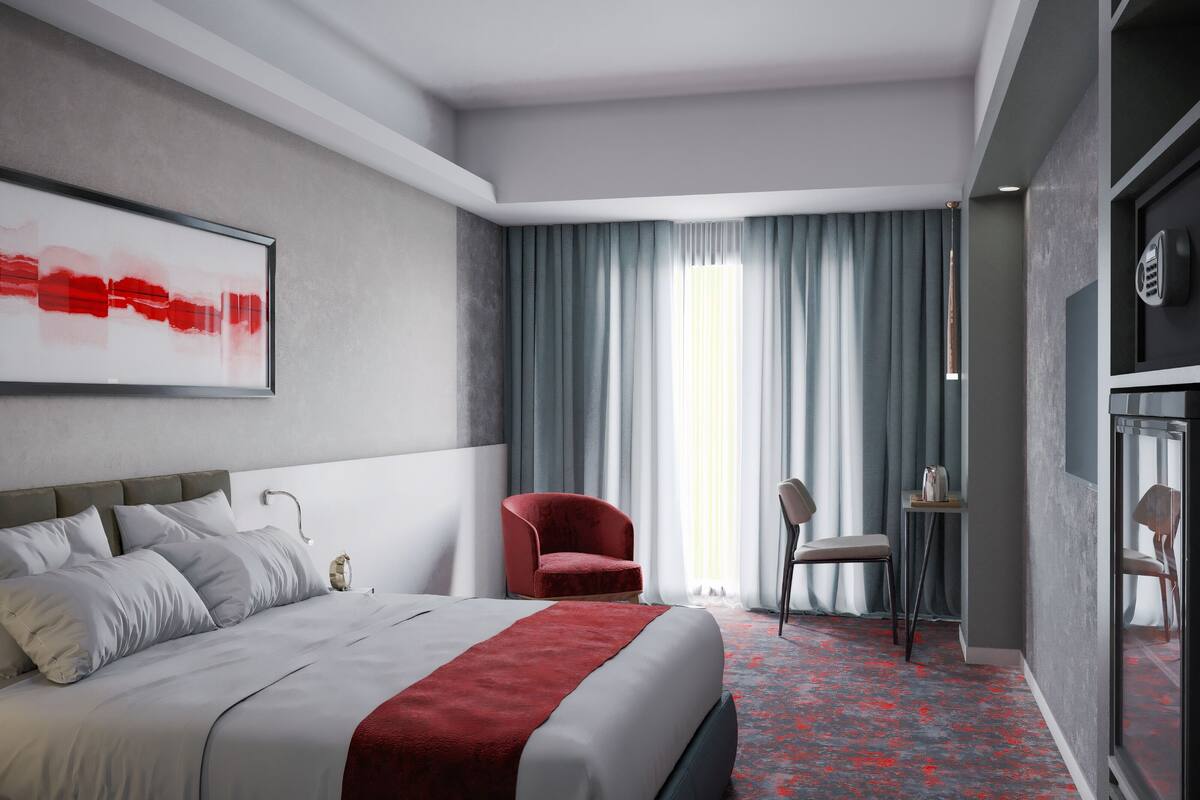 A modern hotel room with a bed, a red armchair, a desk, and a large window with curtains.