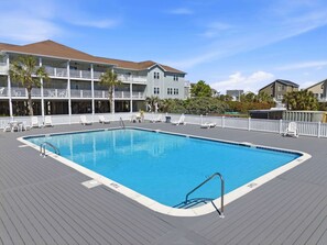 Une piscine avec une terrasse, des chaises longues et une clôture blanche.