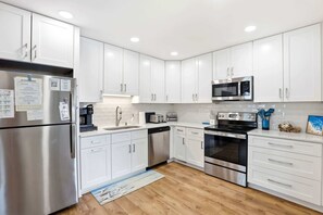 A modern kitchen with white cabinets, stainless steel appliances, and a wooden floor. - Filling Beachy by Brunswick Vacation Rentals: Oceanfront Complex with Pool (Ocean Isle Beach)