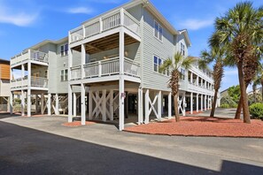 A two-story building with balconies, a covered walkway, and palm trees. - Filling Beachy by Brunswick Vacation Rentals: Oceanfront Complex with Pool (Ocean Isle Beach)