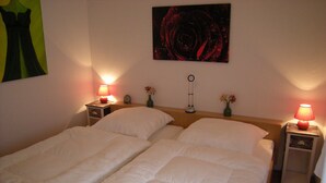 A double bed with white bedding, two bedside tables with lamps, a clock, and a vase with flowers. - Bungalow 23 for up to 4 people at the RHÖN RESIDENCE vacation complex. (Dipperz)