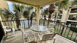 A balcony with a round glass table and white chairs, surrounded by a black metal railing.