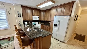 A kitchen with wooden cabinets, a granite countertop, a white refrigerator, and a built-in island with bar stools.