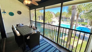 A covered patio with a dining table and chairs, a ceiling fan, and a view of a swimming pool and palm trees. - Beautifully upgraded Gold-rated unit, where style meets comfort. (Saint Augustine)