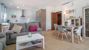 Un salon moderne avec un canapé gris, une table basse sur laquelle sont posés des livres et un coin repas comprenant une table et des chaises en bois.