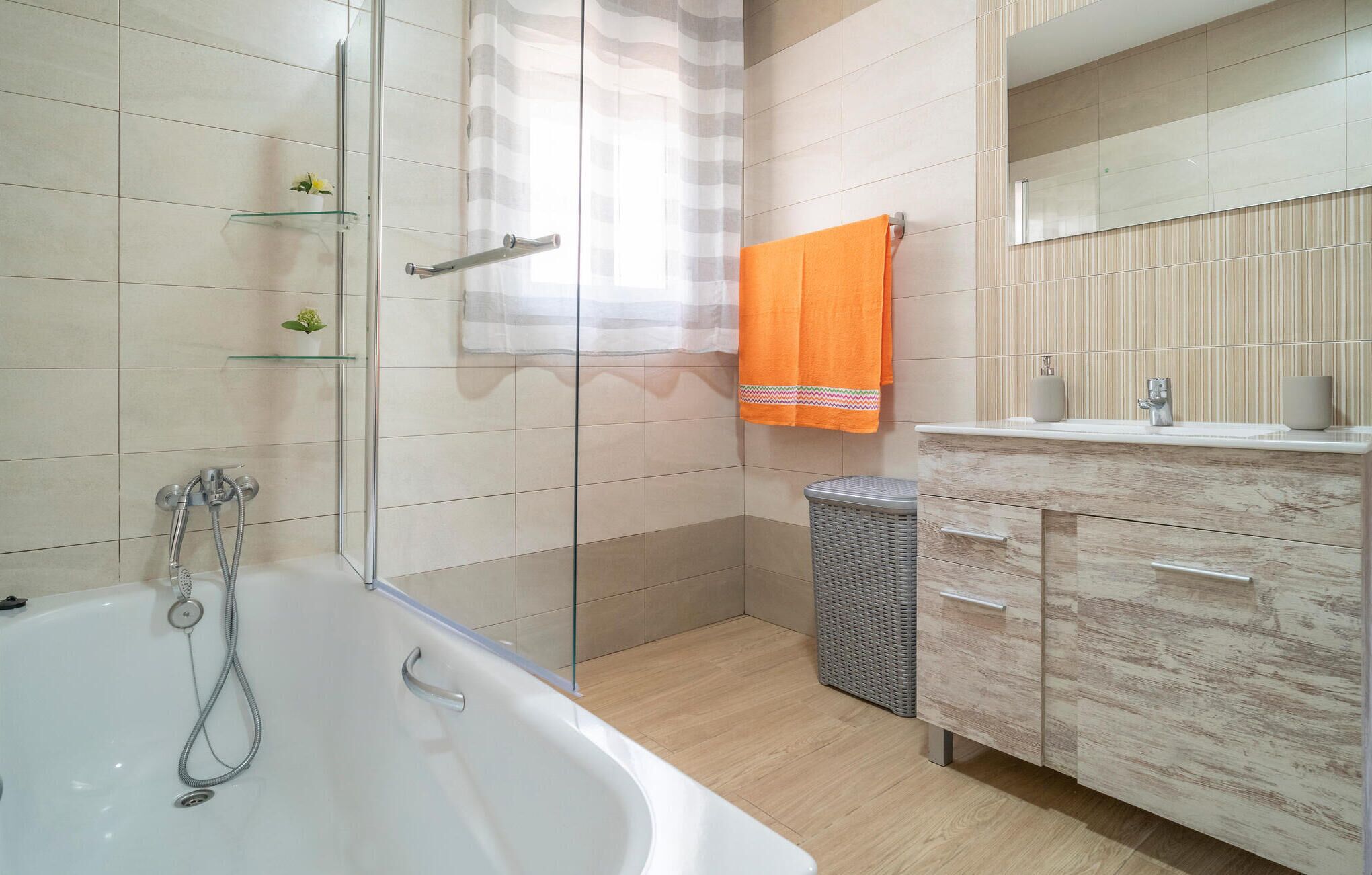 Ein modernes Badezimmer mit Badewanne, Duschkabine aus Glas, einem Korbwannenkorb und einem Holzwaschtisch mit Spiegel.