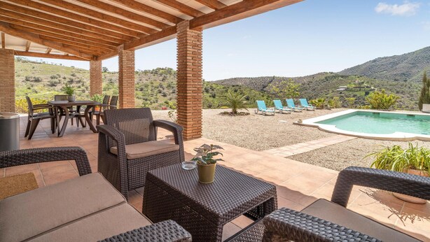 Une terrasse couverte aménagée avec des meubles en osier, une piscine et une vue sur les collines.