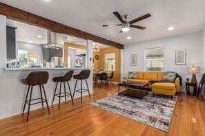 A modern living room with a yellow sofa, a coffee table, and a bar area with stools. - Coronado Cool, Banner Close, Cozy Vibes Sleeps 4 (Phoenix)
