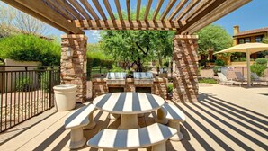 Eine Terrasse im Freien mit einer Pergola, Steinpfeilern, einem runden Tisch mit Bänken und einem Grill.