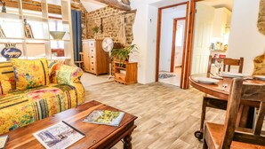 Uma sala de estar acolhedora com uma mesa de centro de madeira, um sofá colorido e uma área de jantar com mesa e cadeiras de madeira.