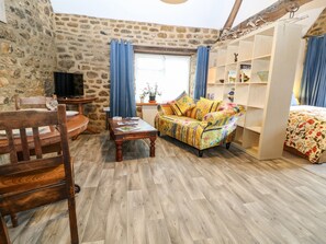 Une pièce chaleureuse avec un mur en pierre, une table à manger en bois entourée de chaises, un canapé agrémenté de coussins colorés, une bibliothèque et une fenêtre ornée de rideaux bleus.
