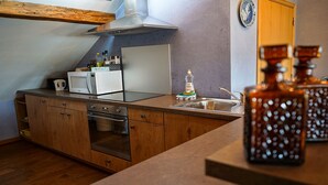 Eine kompakte Küche mit Holzausbau, einem Einbauofen, einer Mikrowelle und einer Edelstahl-Spüle.