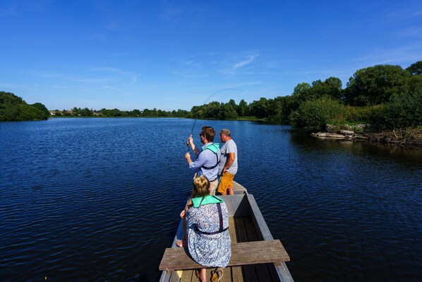 A wooden boat on a calm river with people fishing.
