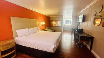 A hotel room with a large bed, a desk, a chair, and a television.