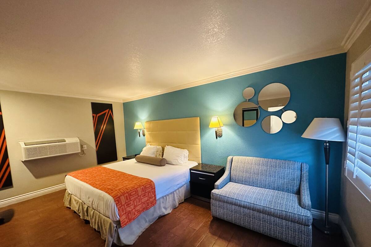 Habitació d'hotel amb llit, una cadira, una tauleta de nit i un mirall fixat a la paret.