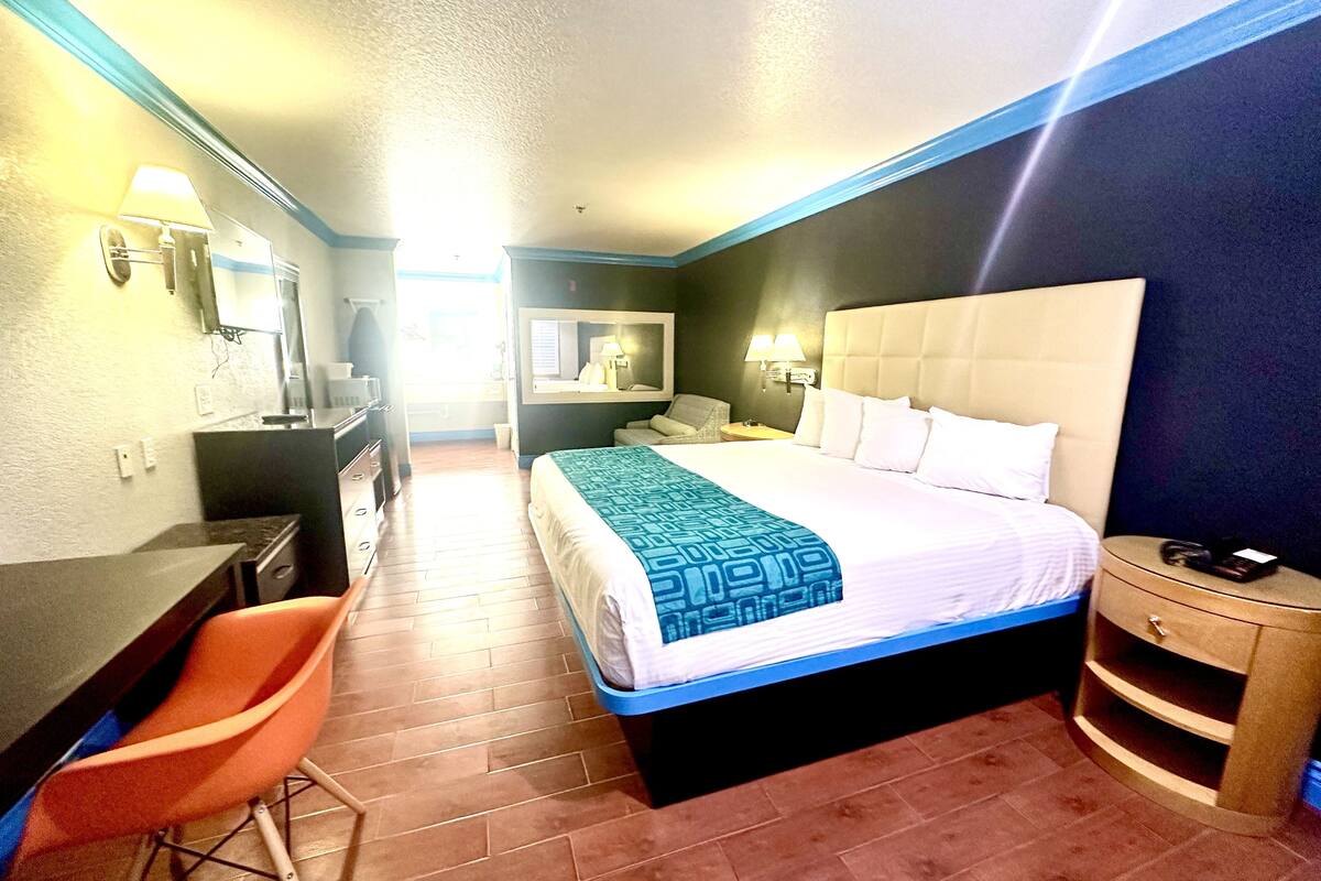 Habitació d'hotel amb un llit, escriptori, cadira, tauleta de nit i un bany visible al fons.