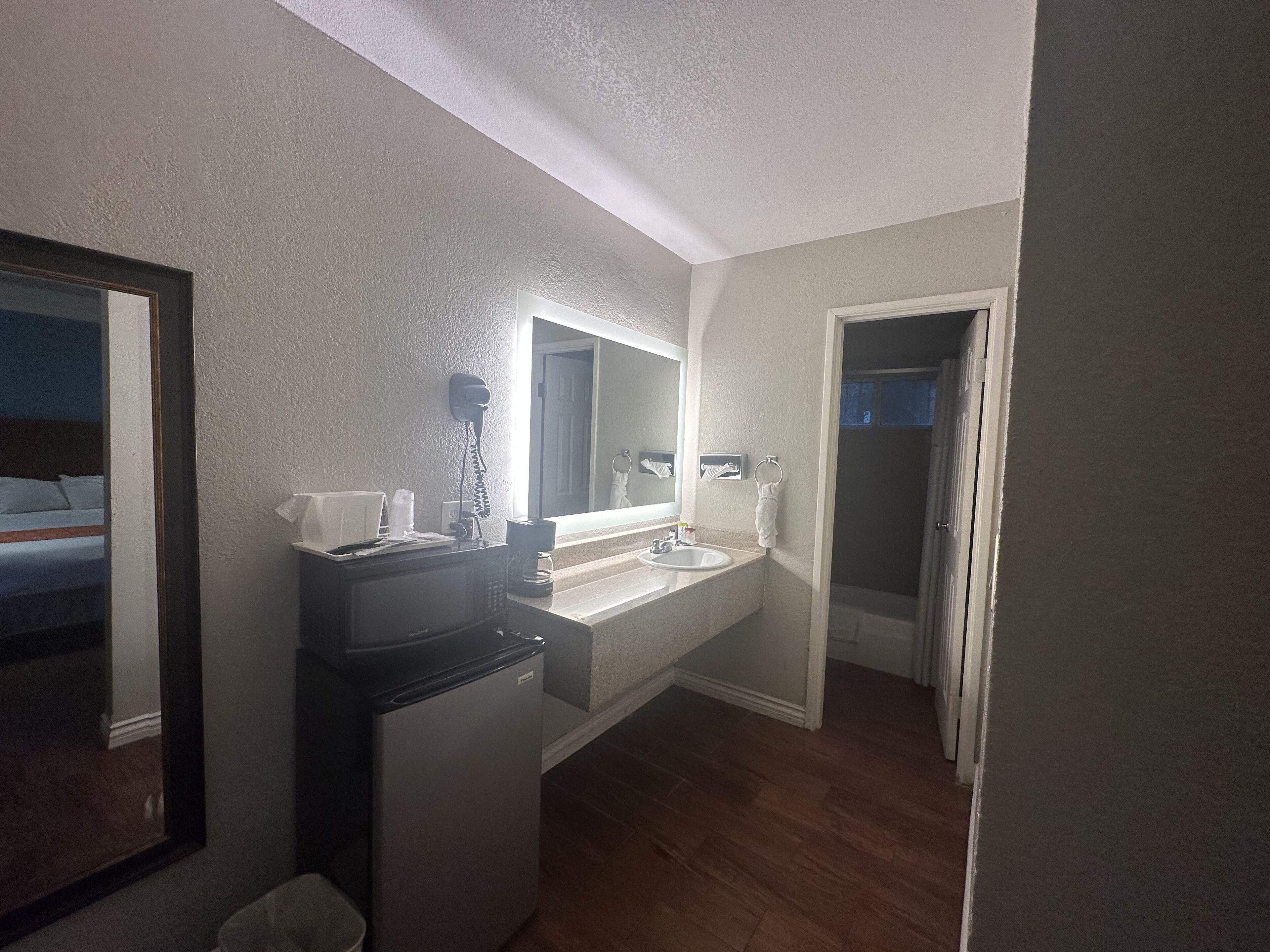A compact bathroom with a sink, mirror, and a small refrigerator.