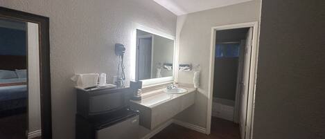 A compact bathroom with a sink, mirror, and a small refrigerator.