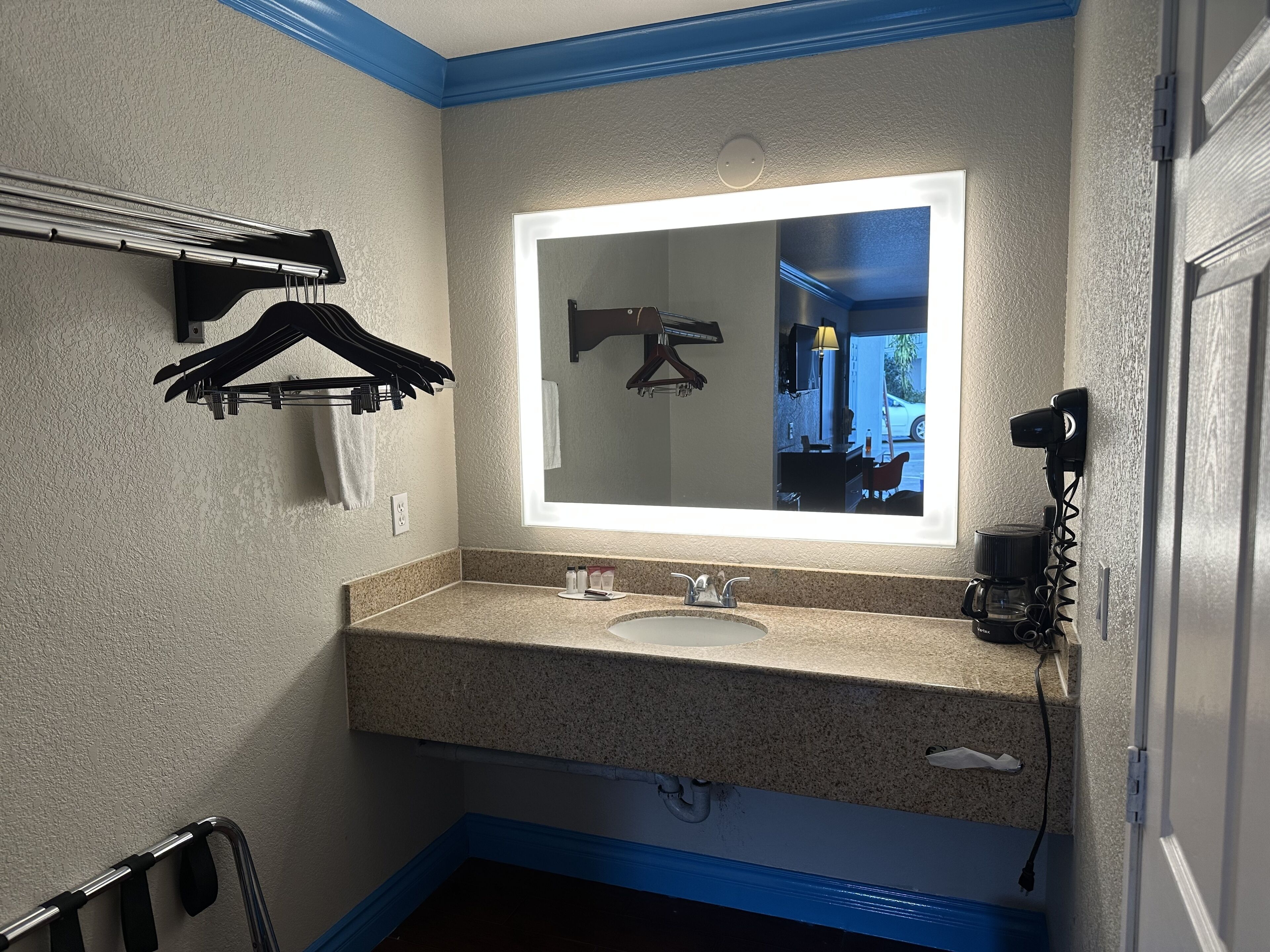 Une salle de bain dotée d’un comptoir en granit, d’un lavabo, d’un miroir avec éclairage intégré, d’un porte-serviettes, d’un sèche-cheveux et d’une tringle pour le rideau de douche.