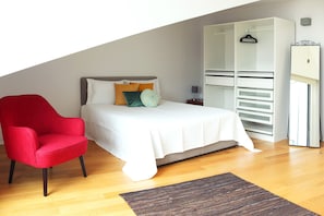 A bedroom with a bed, a red chair, a white wardrobe, and a wooden floor.