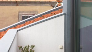 A balcony with a potted plant, a window, and a red-tiled roof in the background. - Villa Invicta II (Porto)