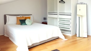 A neatly made bed with white bedding and decorative pillows, a wooden floor, and a white wardrobe with open doors. - Villa Invicta II (Porto)