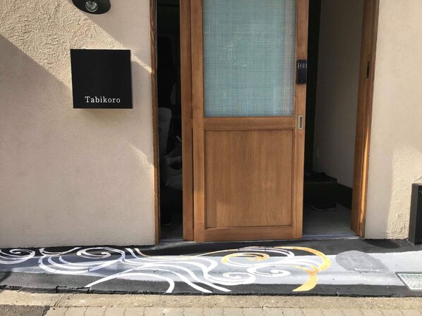 L’entrée d’un hôtel, avec une porte en bois, une plaque portant l’inscription « Tabikoro » et un motif décoratif sur le sol.