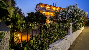 A two-story building with a balcony, surrounded by greenery and a white wall. - Yria ntn Studios (Zakynthos)