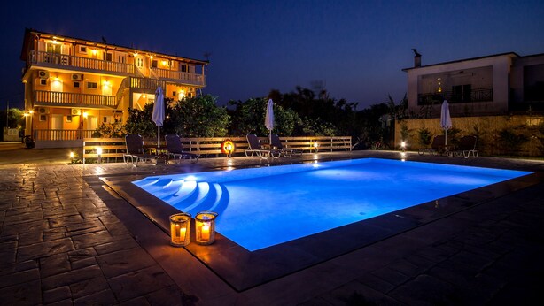A swimming pool with lounge chairs and candles, surrounded by a stone patio and a building with balconies. - Yria ntn Studios (Zakynthos)