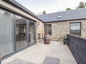 A modern patio with stone walls, a large sliding glass door, and a wooden barrel. - The Steading (Rogart)